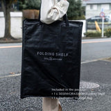 Black folding shelf with '5050WORKSHOP' branding held by a person outdoors.