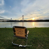 Folding chair with a scenic view of a lake and bridge at sunset.