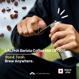 A person grinding coffee with a LALPHA Barista Coffee Mill CK-300. The image features a close-up of the hands operating the silver and black metal coffee mill, with floating coffee beans on the left and promotional text overlays at the bottom.