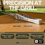 A stainless steel culinary divider tool branded LALPHA rests on a wooden surface with a blurred campsite background. Large text reads 'PRECISION AT THE GRILL.