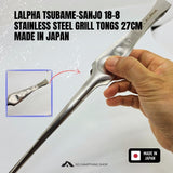 A hand holding a stainless steel grill tong for lamb chops, with product text reading 'LALPHA TSUBAME-SANJO 18-8 STAINLESS STEEL GRILL TONGS 27CM MADE IN JAPAN' and a small inset showing the tip detail.