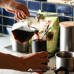 Person pouring coffee into a jar with coffee beans and a bag of coffee in the background.