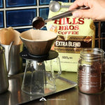 Person pouring coffee grounds into a filter with Hills Bros Coffee bag in the background